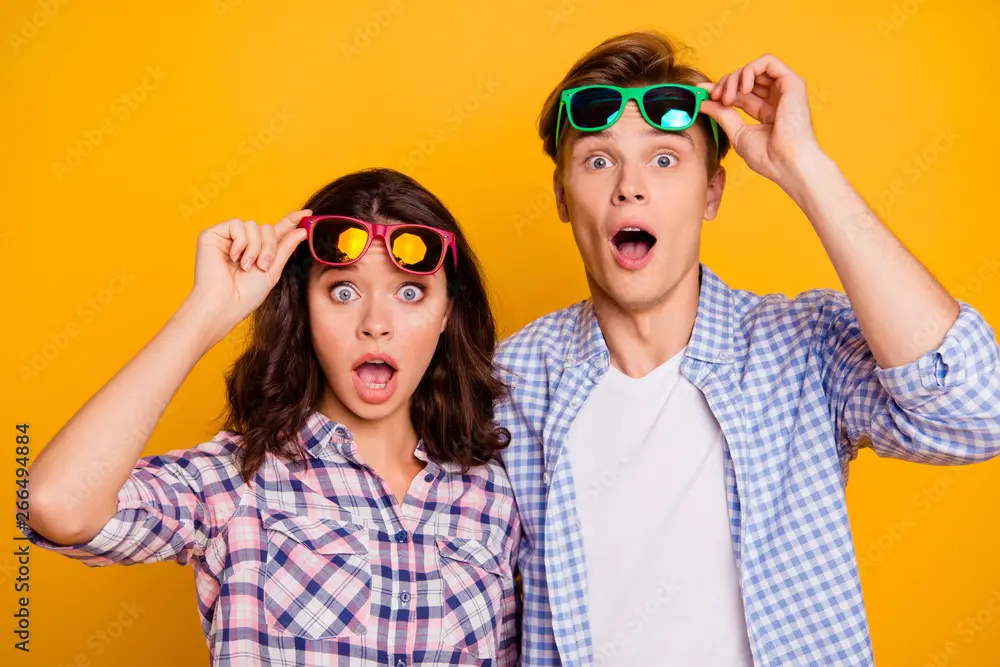 Close up photo of pair in raised up summer glasses specs he him his she her lady boy showing shock staring  with open eyes and mouth wearing casual plaid shirts outfit isolated on yellow background